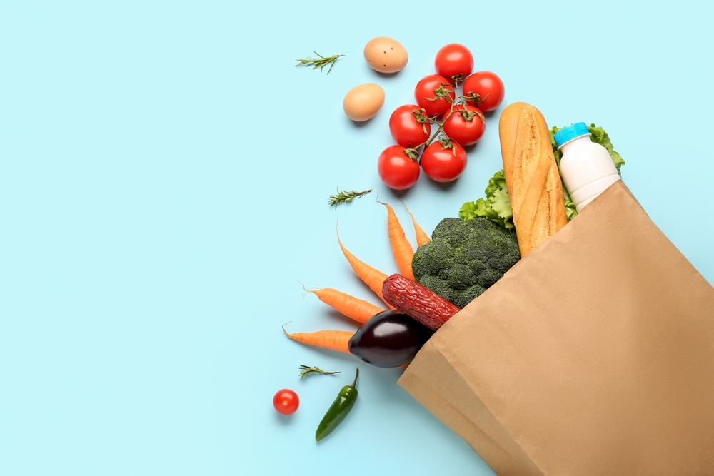 A paper grocery bag spilling tomatoes, carrots, bread and milk