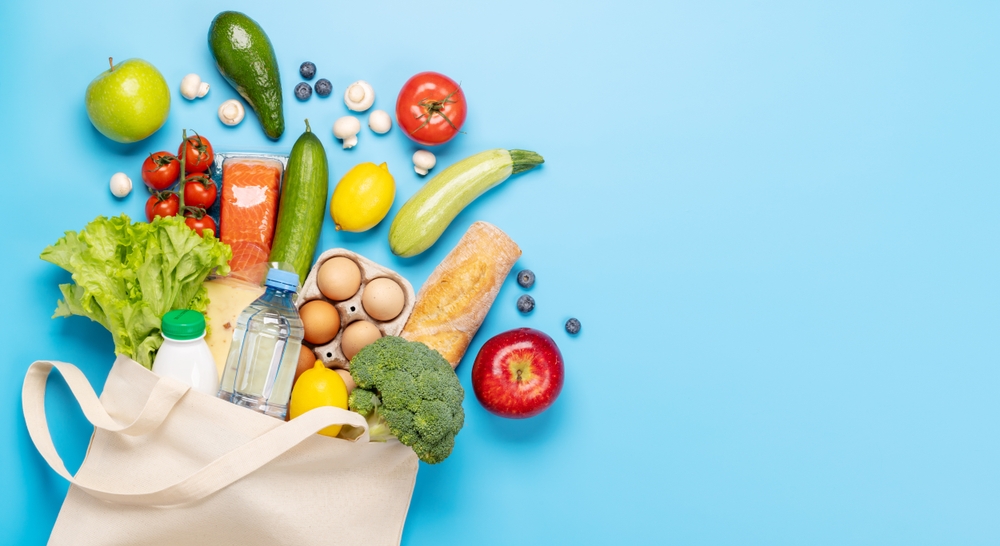 A canvas tote spilling eggs, fresh bread, greens and vegetables